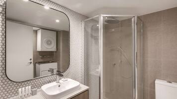 Un baño moderno con ducha envuelta en vidrio, un espejo grande y un lavamanos blanco.