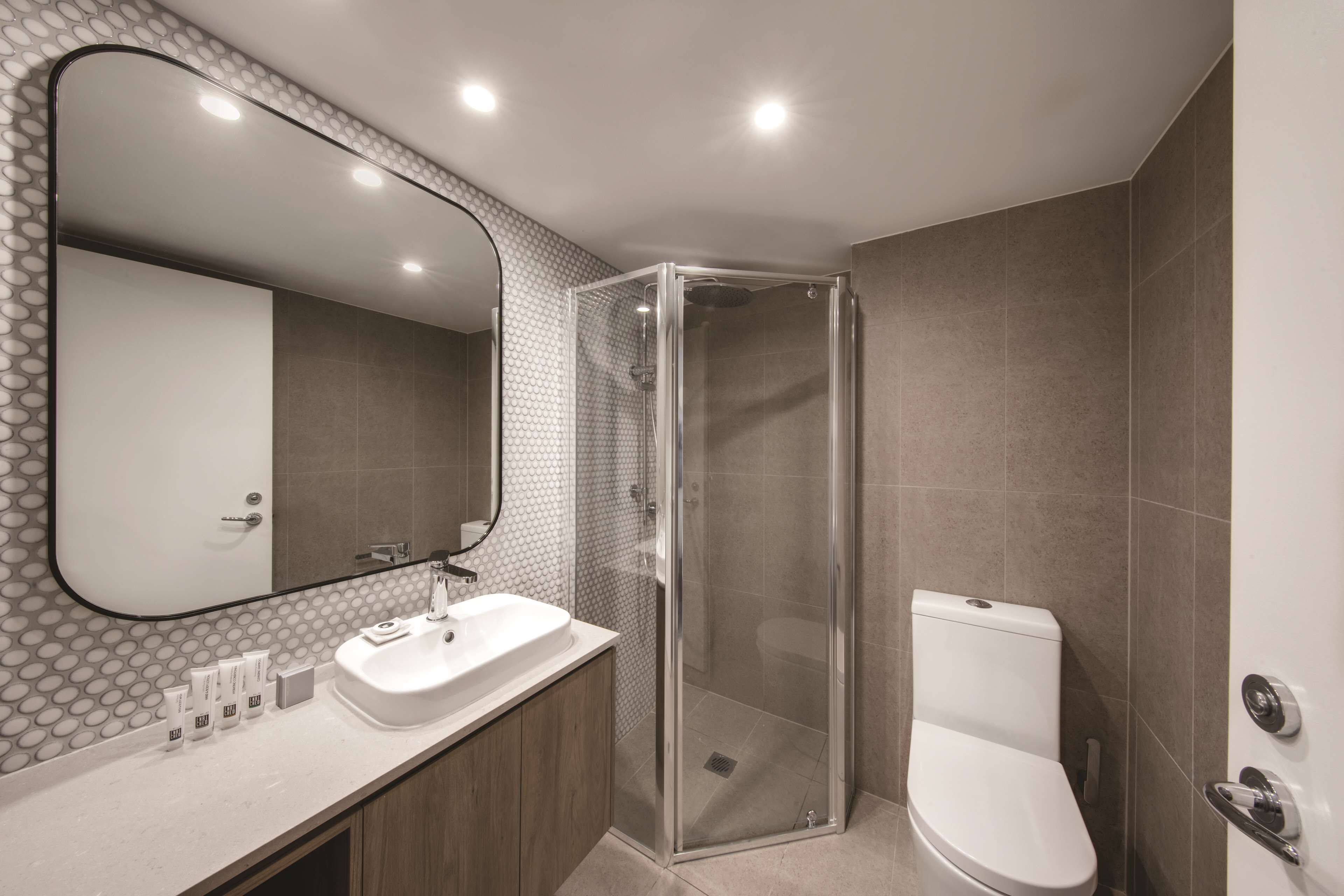 A modern bathroom with a glass-enclosed shower, a large mirror, and a white sink.