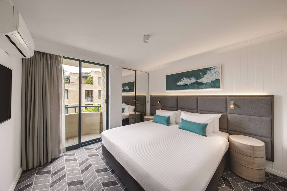 Een moderne hotelkamer met een groot bed, een klein nachtkastje, een spiegel en uitzicht op het balkon.