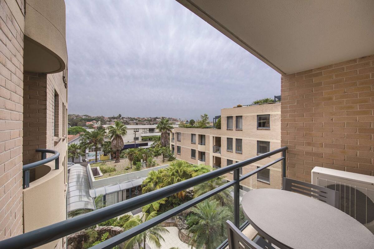 Een balkon met uitzicht op een binnentuin, met palmbomen en een gebouw met een bakstenen gevel.