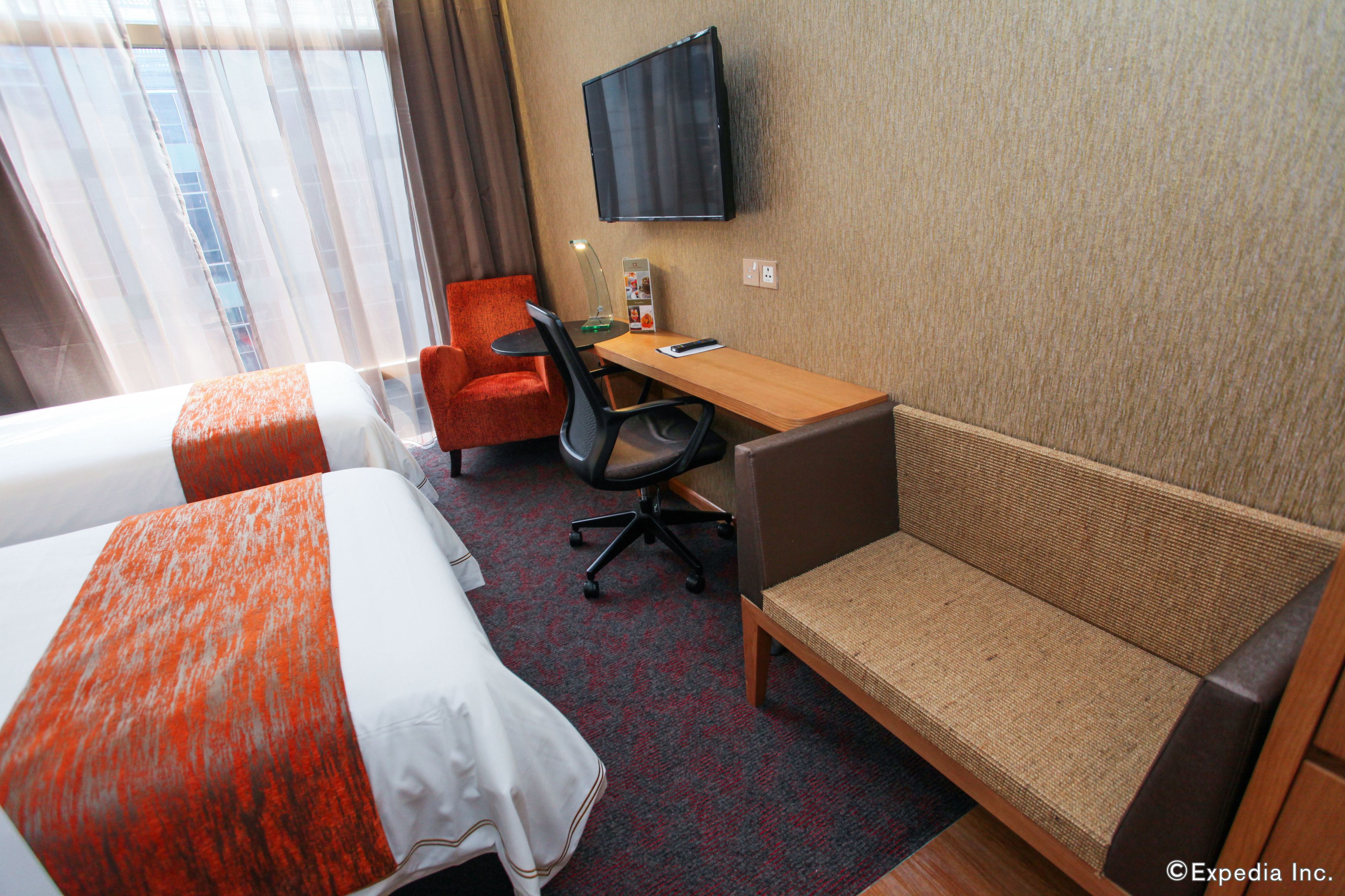 Habitación de hotel con dos camas, un escritorio, una silla, un televisor y una ventana con cortinas.