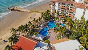 Hotel na praia com piscina, palmeiras e vista para o oceano.