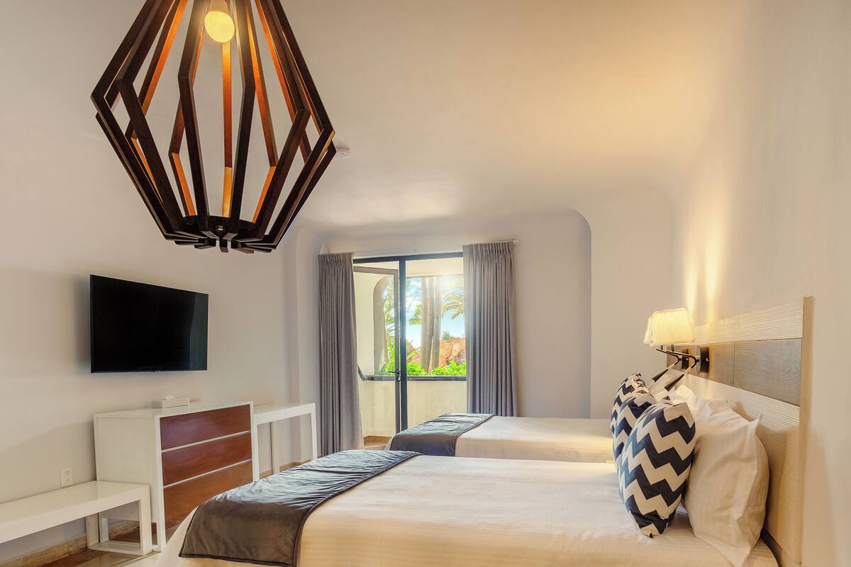 A hotel room with a bed, a TV, a desk, and a large window with curtains.