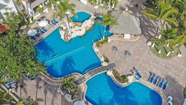 Vista aérea de um resort com várias piscinas, palmeiras e áreas de descanso.