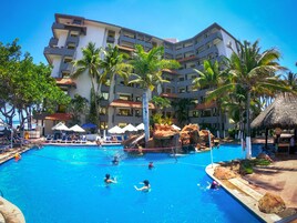 Un hotel con piscina, palmeras y una estructura de techo de paja.