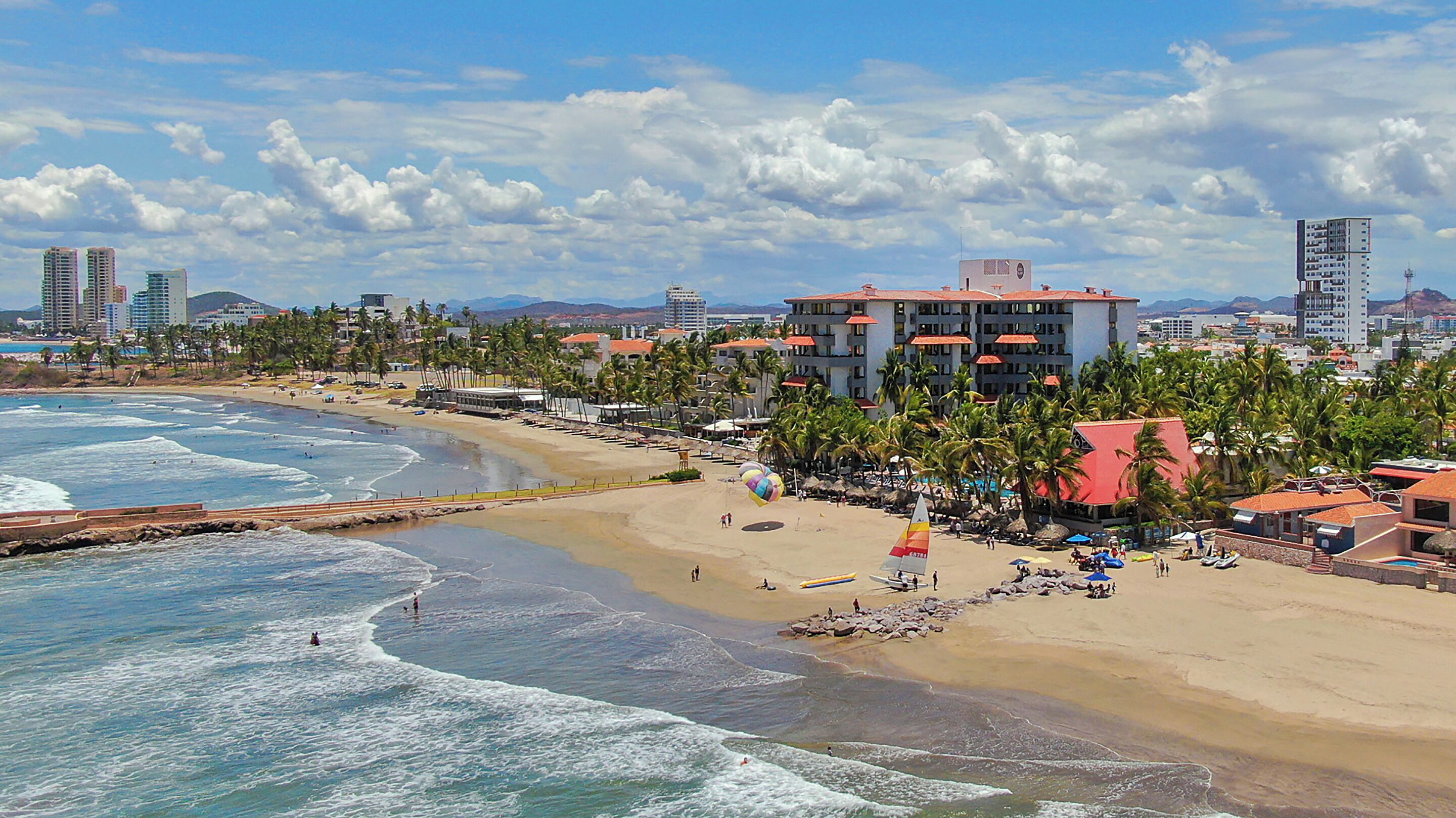 A coastal cityscape with a beach, palm trees, and high-rise buildings.