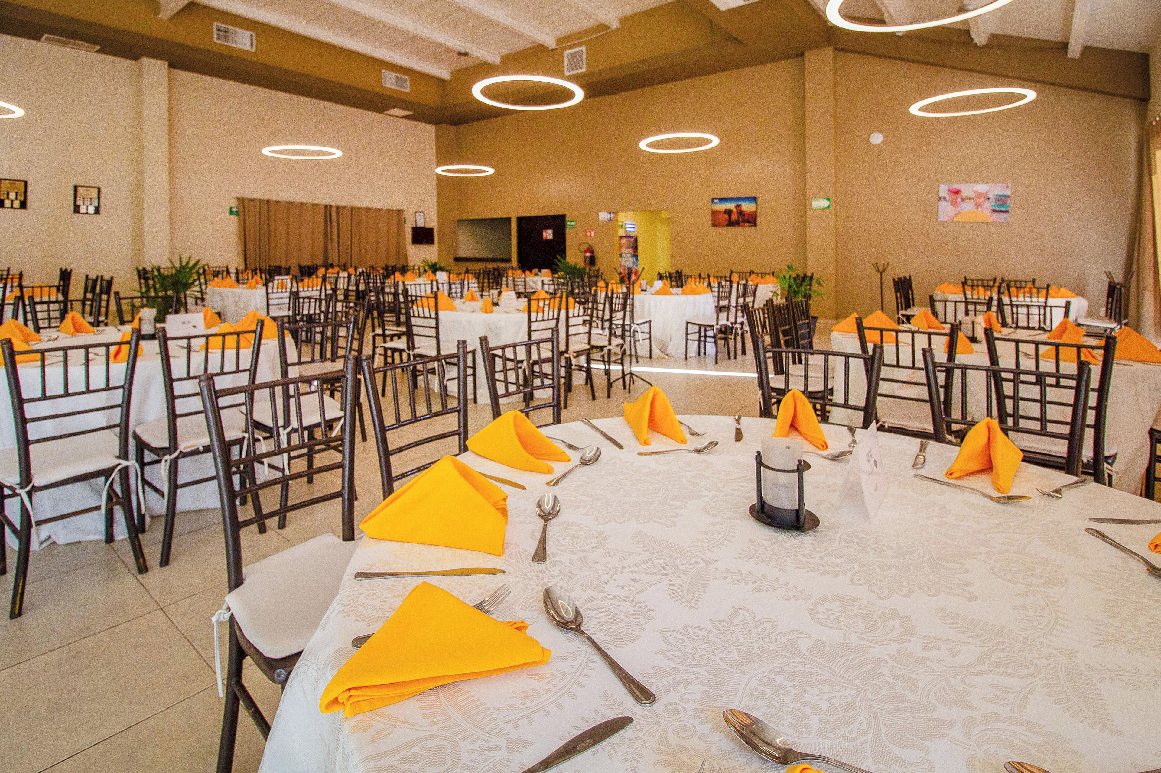 Une salle de banquet avec des tables rondes, des chaises et des serviettes de table orange.