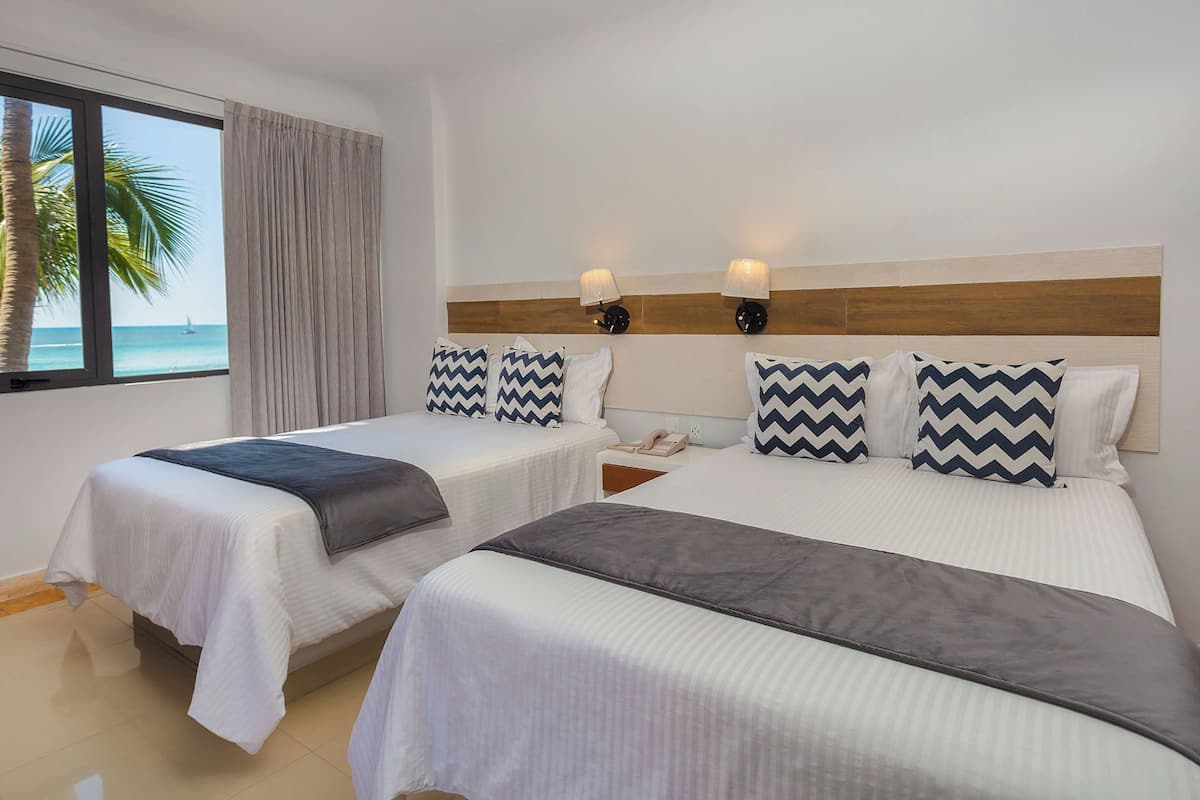 A hotel room with two beds, a view of the ocean, and a wooden headboard.