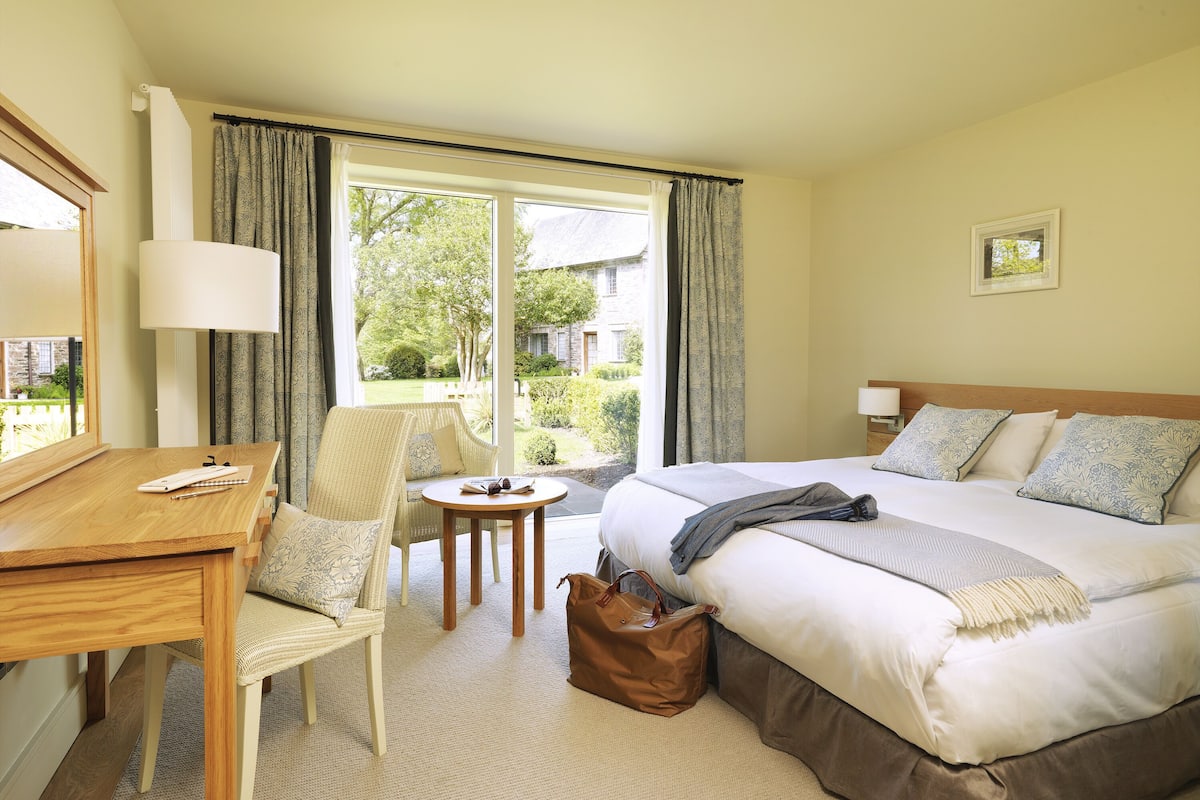 A hotel room with a bed, a desk, a chair, a small table, and a view of the outdoors.