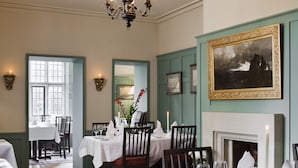 A dining room with tables set for a meal, a fireplace, and framed artwork on the walls.