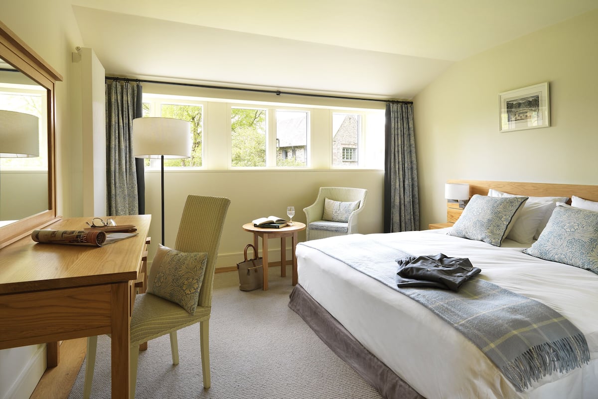 A hotel room with a bed, a desk, a chair, a small table, and a window with curtains.