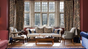 A room with a large bay window, a sofa set, two armchairs, a coffee table, and a patterned rug.
