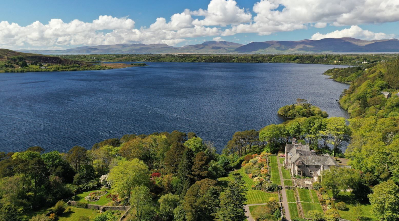A large lake with a house surrounded by lush greenery and mountains in the background.