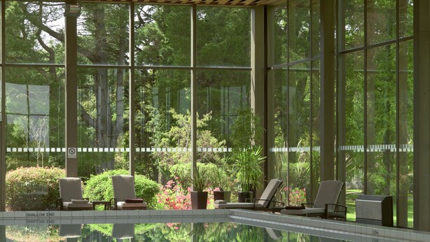 A swimming pool with lounge chairs and a view of a lush garden through large windows. - The Dunloe Hotel & Gardens (Dunloe Lower)