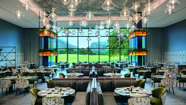 A spacious restaurant with multiple dining areas, large windows offering a view of the outdoors, and hanging pendant lights. - The Dunloe Hotel & Gardens (Dunloe Lower)