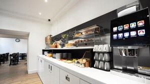 Eine moderne Frühstückstheke mit digitaler Menüanzeige, einer Kaffeemaschine und einer Auswahl an Frühstücksangeboten.