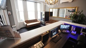 Ein modernes Büro mit Schreibtisch, Computer und Audioausstattung. Zwei Sofas und ein großer Spiegel sind ebenfalls vorhanden.