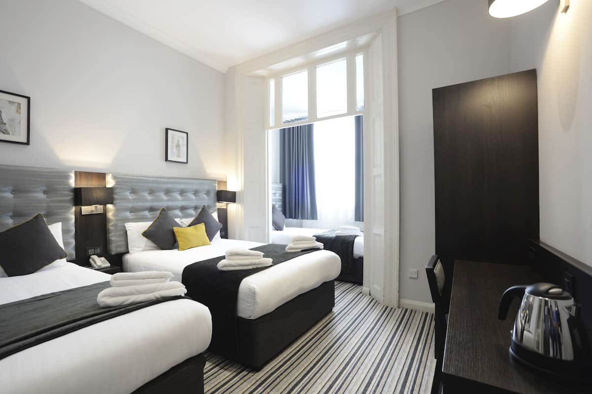 Ein Hotelzimmer mit zwei Betten, einem Schreibtisch, einem Wasserkocher und einem Fenster mit Vorhängen.
