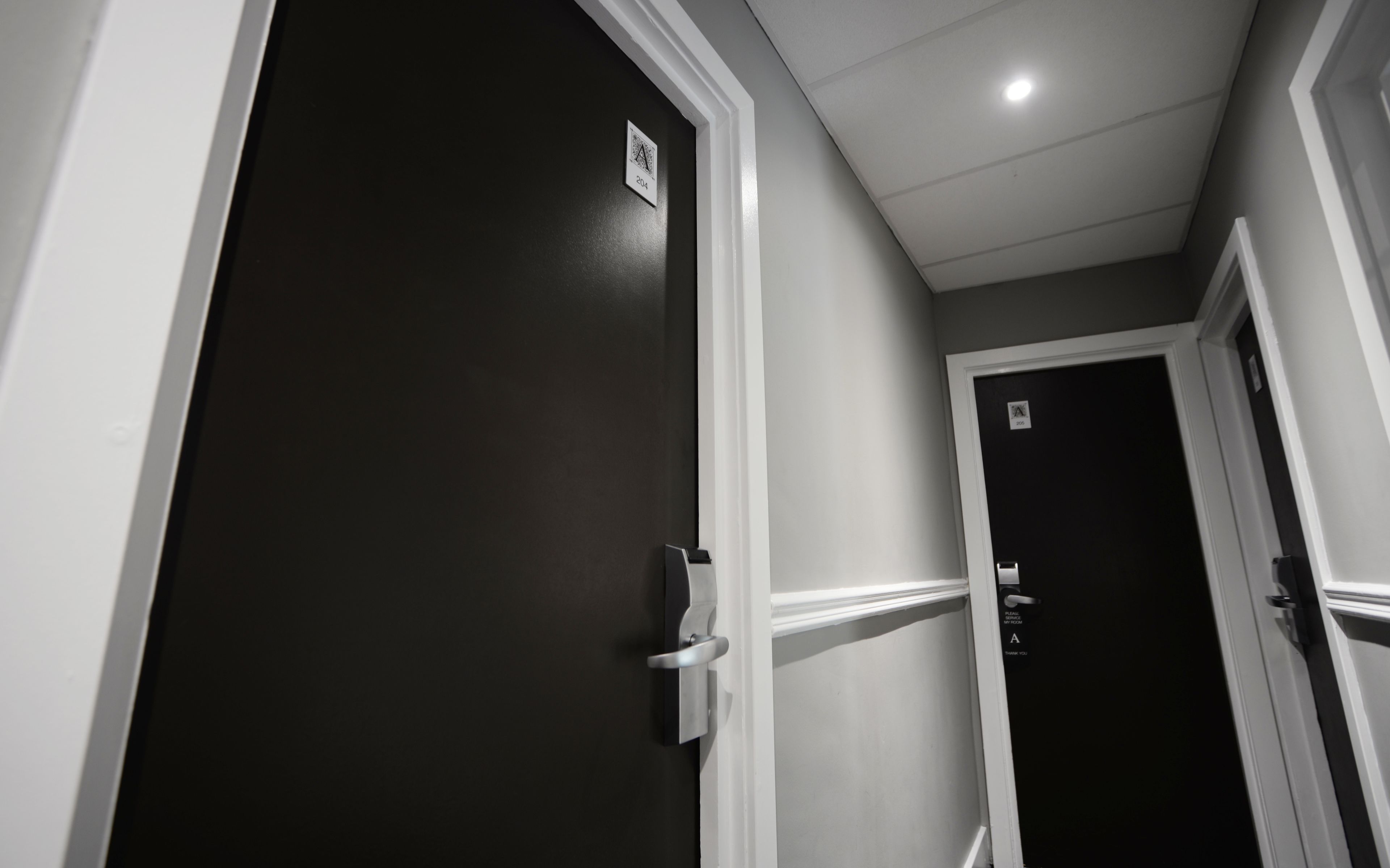 Um corredor com uma porta escura e uma porta mais clara, ambas com moldura branca.