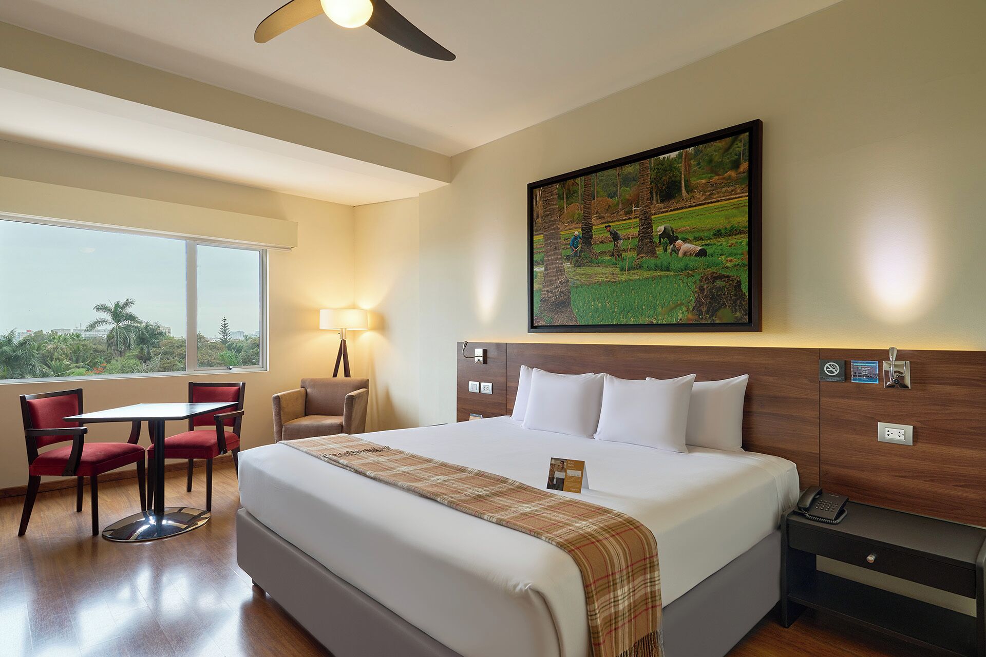 A hotel room with a large bed, a desk, a chair, a lamp, and a painting on the wall.