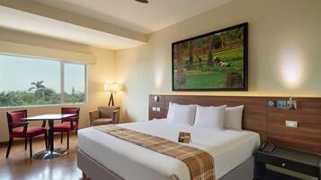 A hotel room with a large bed, a desk, a chair, a lamp, and a painting on the wall.