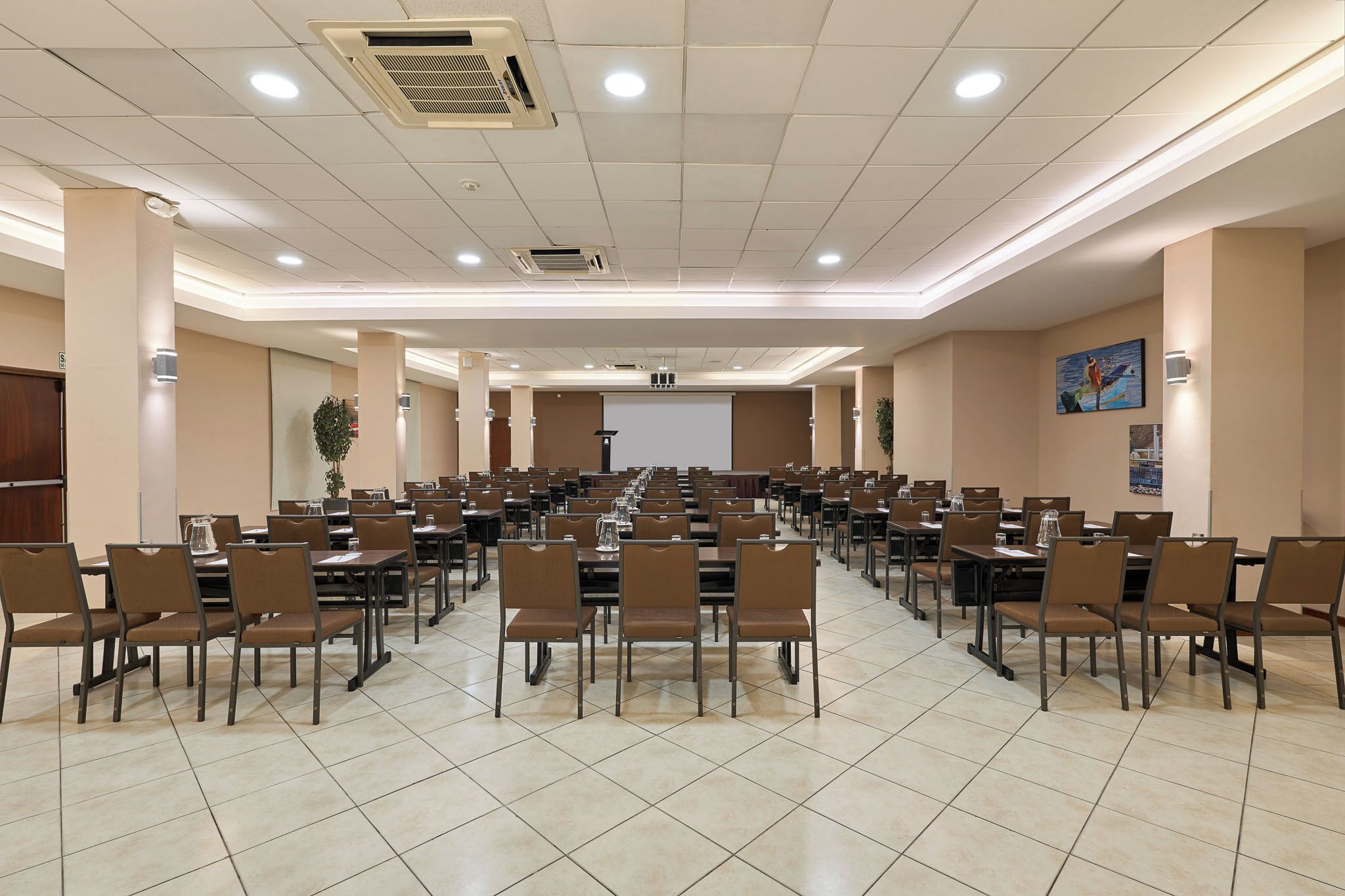 A conference room with rows of tables and chairs, a projector screen, and a large window.
