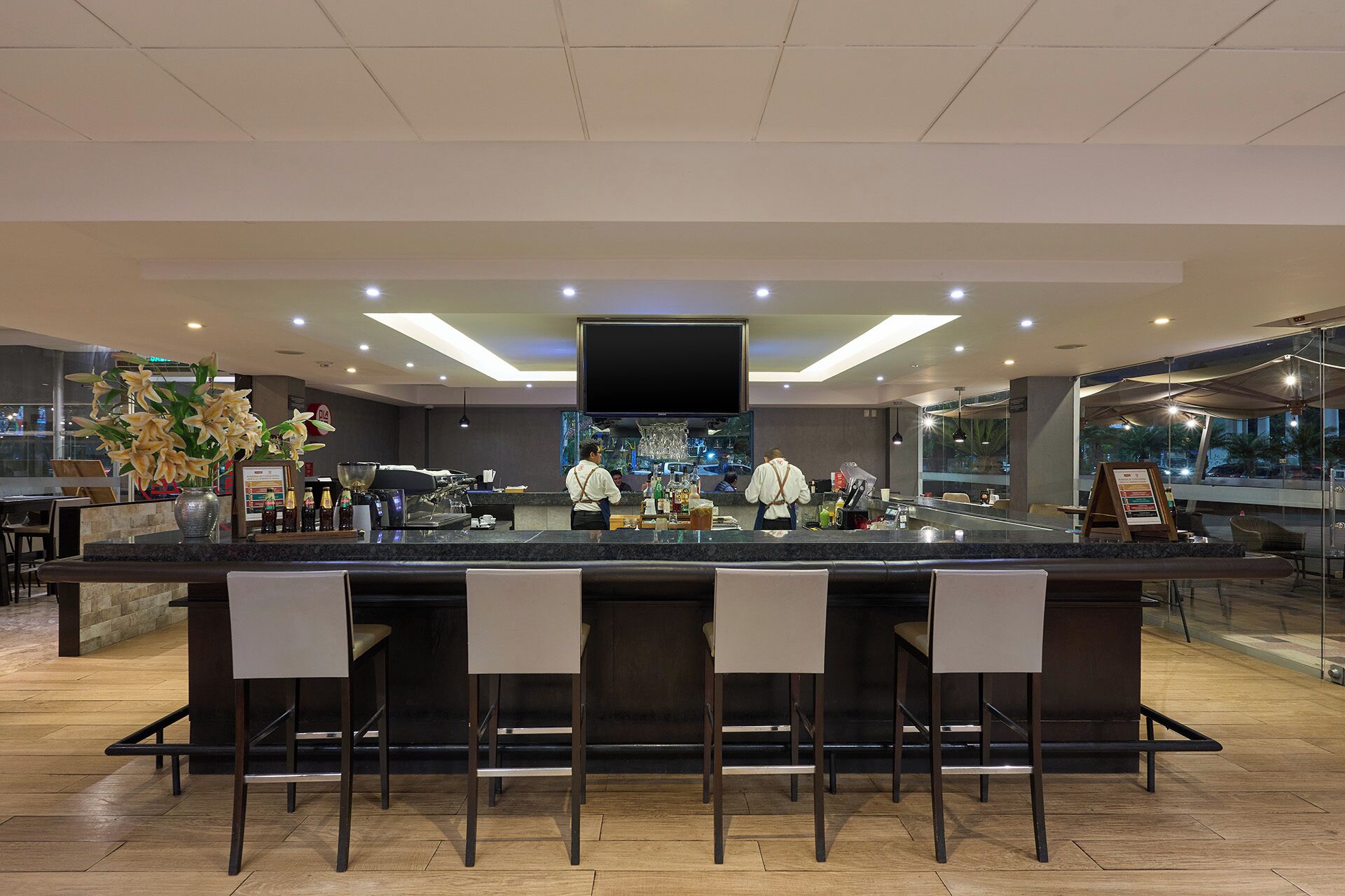 A modern bar area with a flat-screen TV, bar stools, and a counter with a coffee machine.
