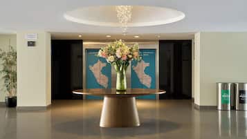 A lobby with a round wooden table, a floral centerpiece, a map of Peru, and recycling bins.