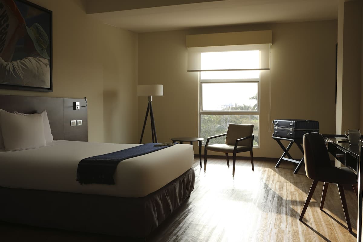 A hotel room with a bed, desk, chairs, and a large window.