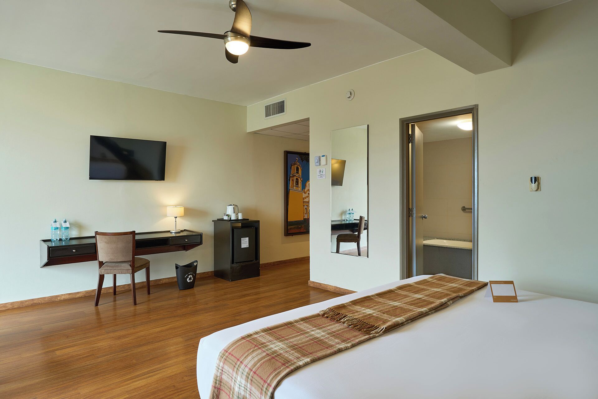 A hotel room with a bed, desk, chair, television, and a door leading to a bathroom.