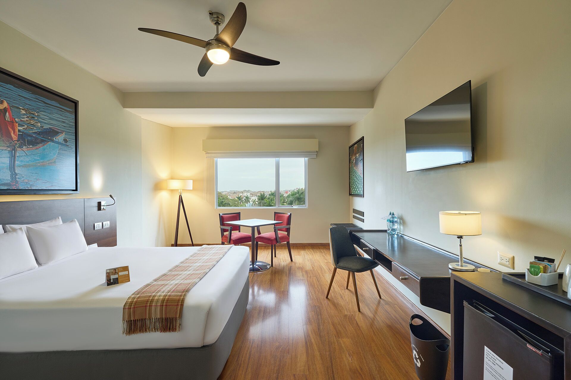 Habitación de hotel con cama, escritorio, silla, televisor y ventilador de techo.
