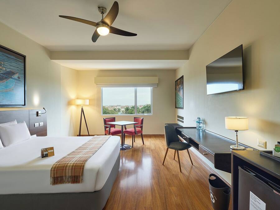 Habitación de hotel con cama, escritorio, silla, televisor y ventilador de techo.