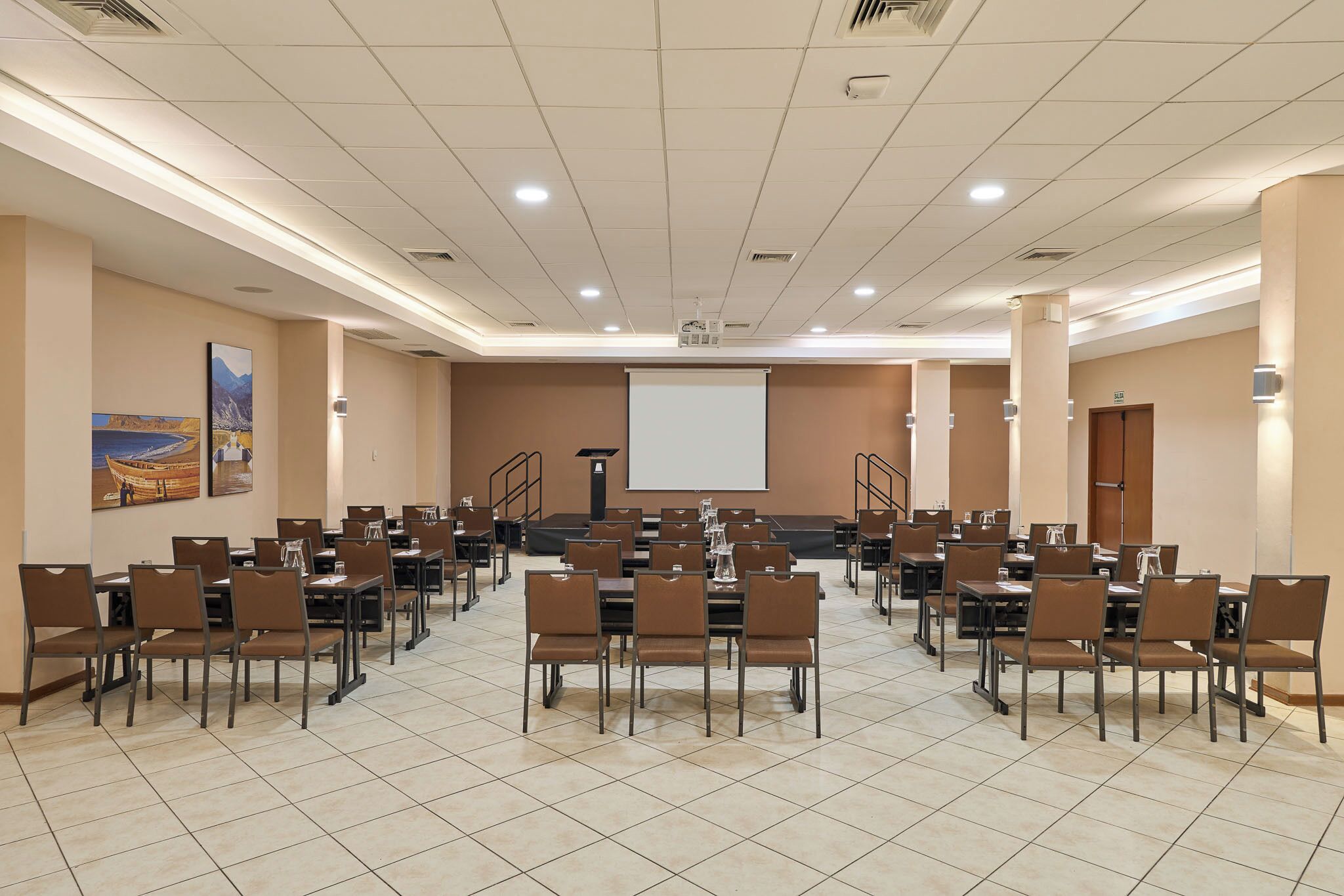 A conference room with multiple tables and chairs, a projector screen, and a large window.