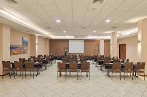 Un salón de conferencias con varias mesas y sillas, una pantalla de proyector y un ventanal grande.