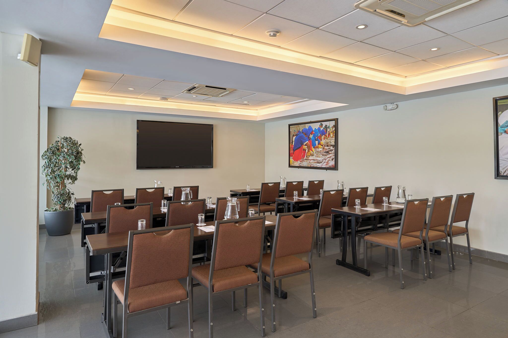 Un salón de conferencias con mesas, sillas, un televisor de pantalla plana grande y una planta en maceta.