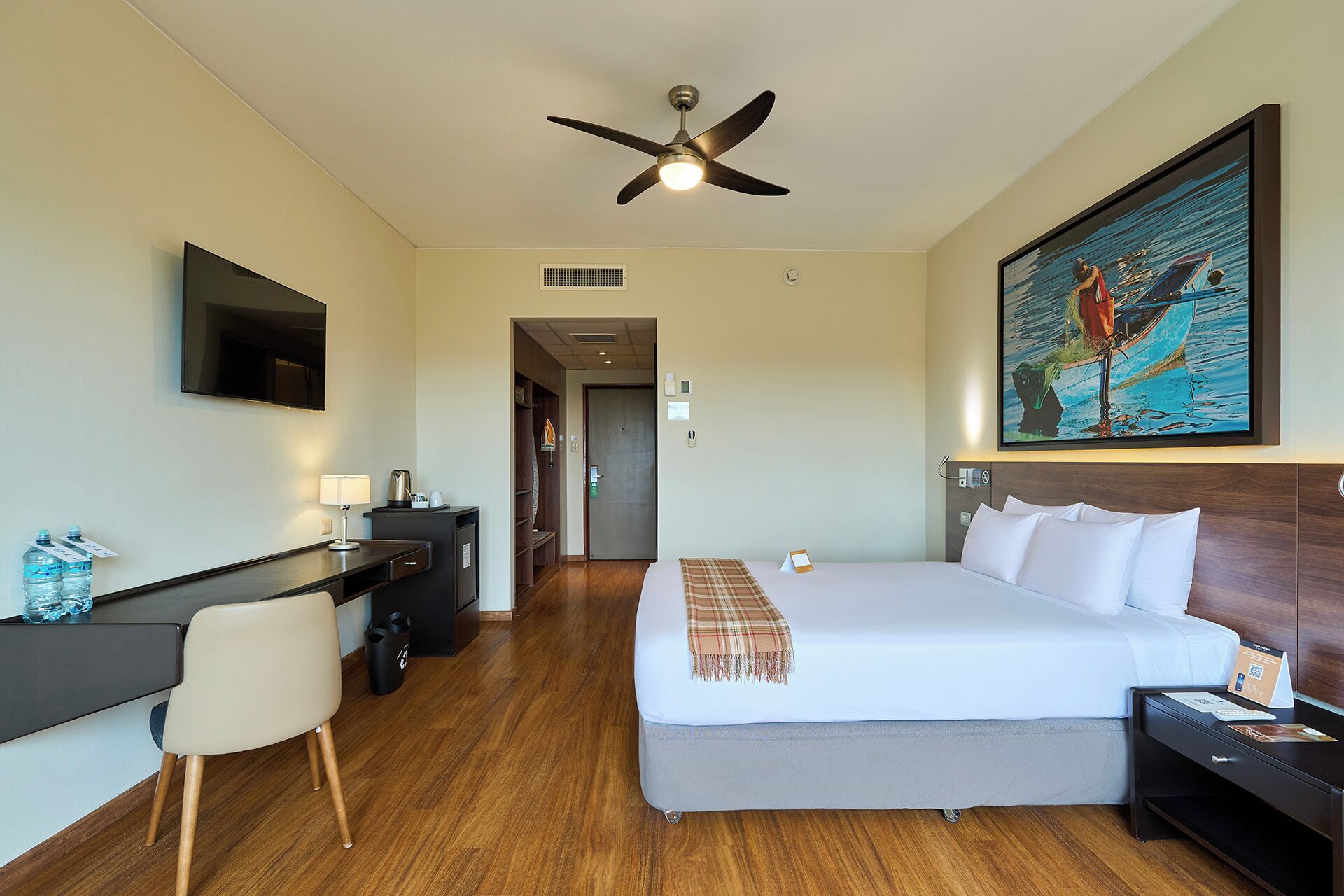 Ein Hotelzimmer mit Bett, Schreibtisch, Stuhl und Deckenventilator.