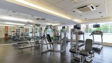 Een sportschool met diverse fitnessapparaten, grote ramen en een spiegelwand.