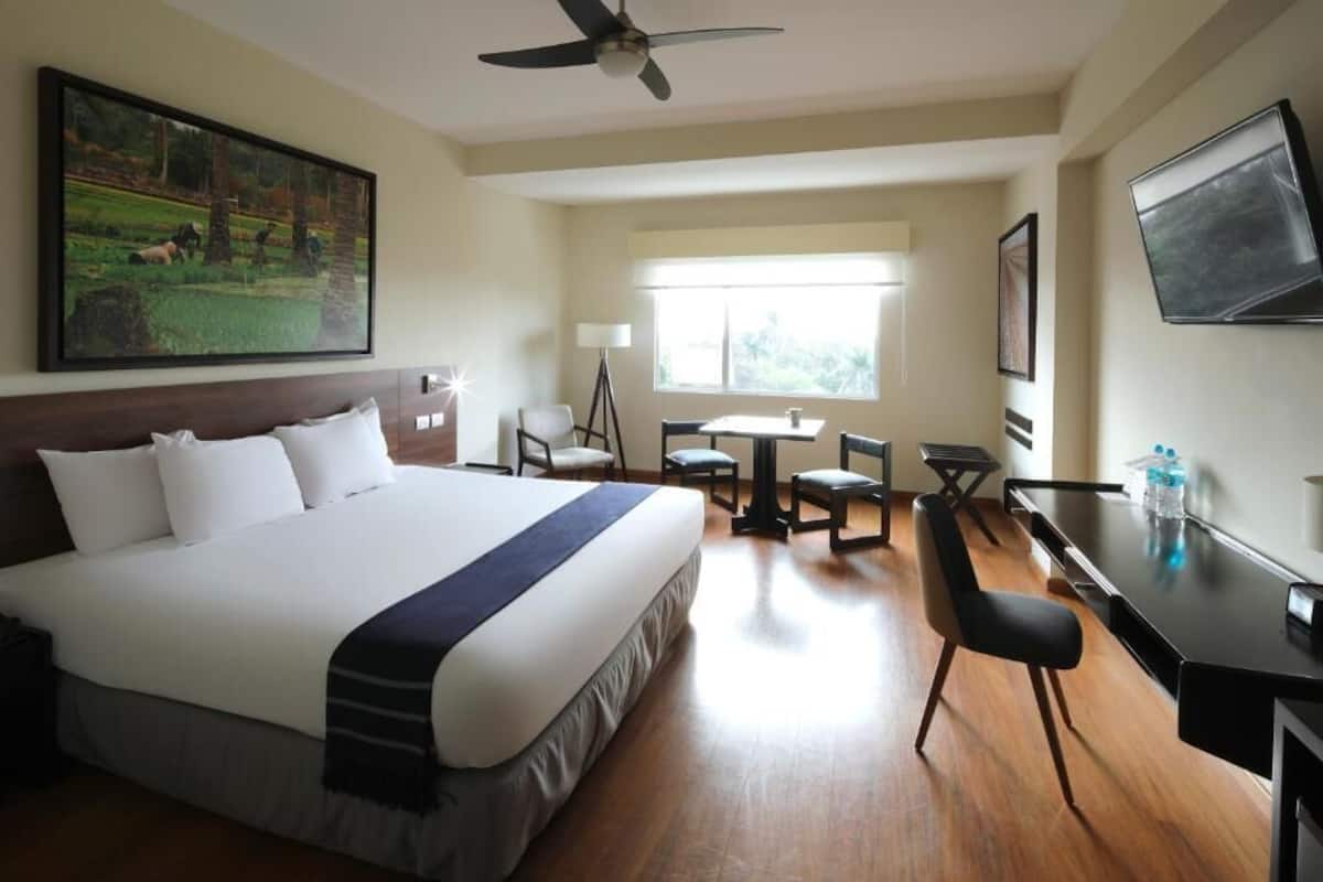 A hotel room with a large bed, a desk, a chair, a TV, and a painting on the wall.