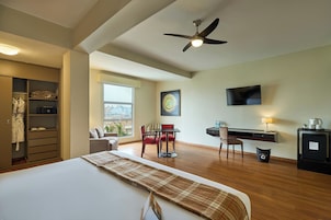 Habitación de hotel con cama, escritorio, silla, televisor y vista a la ciudad.