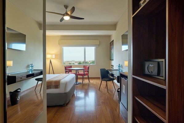 Habitación de hotel con cama, escritorio, silla, mesa de comedor, ventilador de techo, ventana con vistas y minibar.