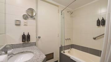 Un baño con lavamanos de encimera de granito, ducha con mampara de vidrio y dos botellas de champú.