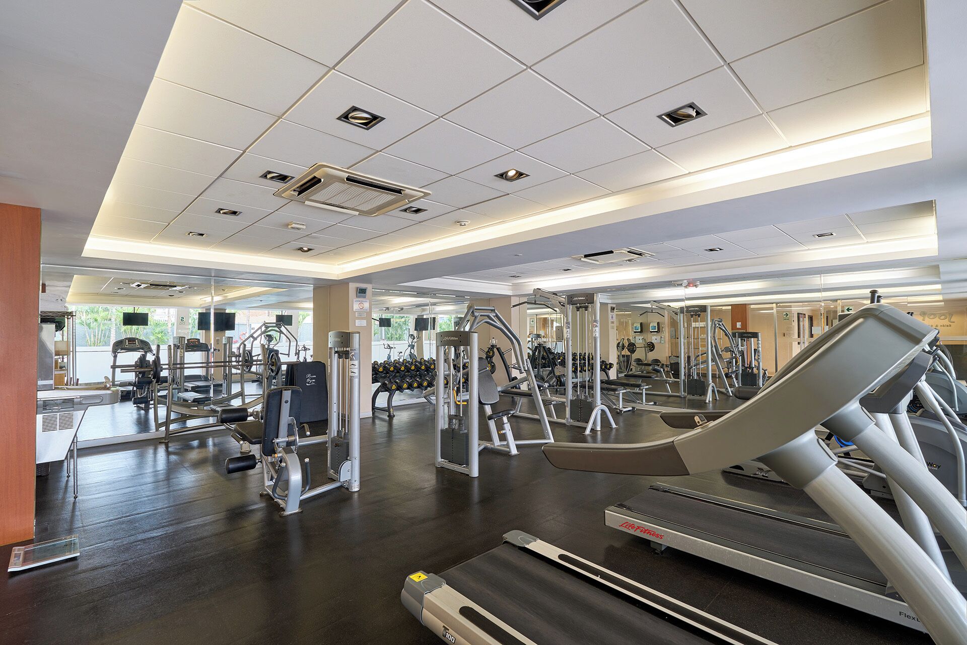 Un gimnasio con cintas de correr, máquinas de pesas y espejos.