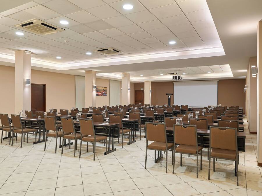 Una sala de conferències amb diverses taules i cadires, una pantalla de projector i una pissarra gran.