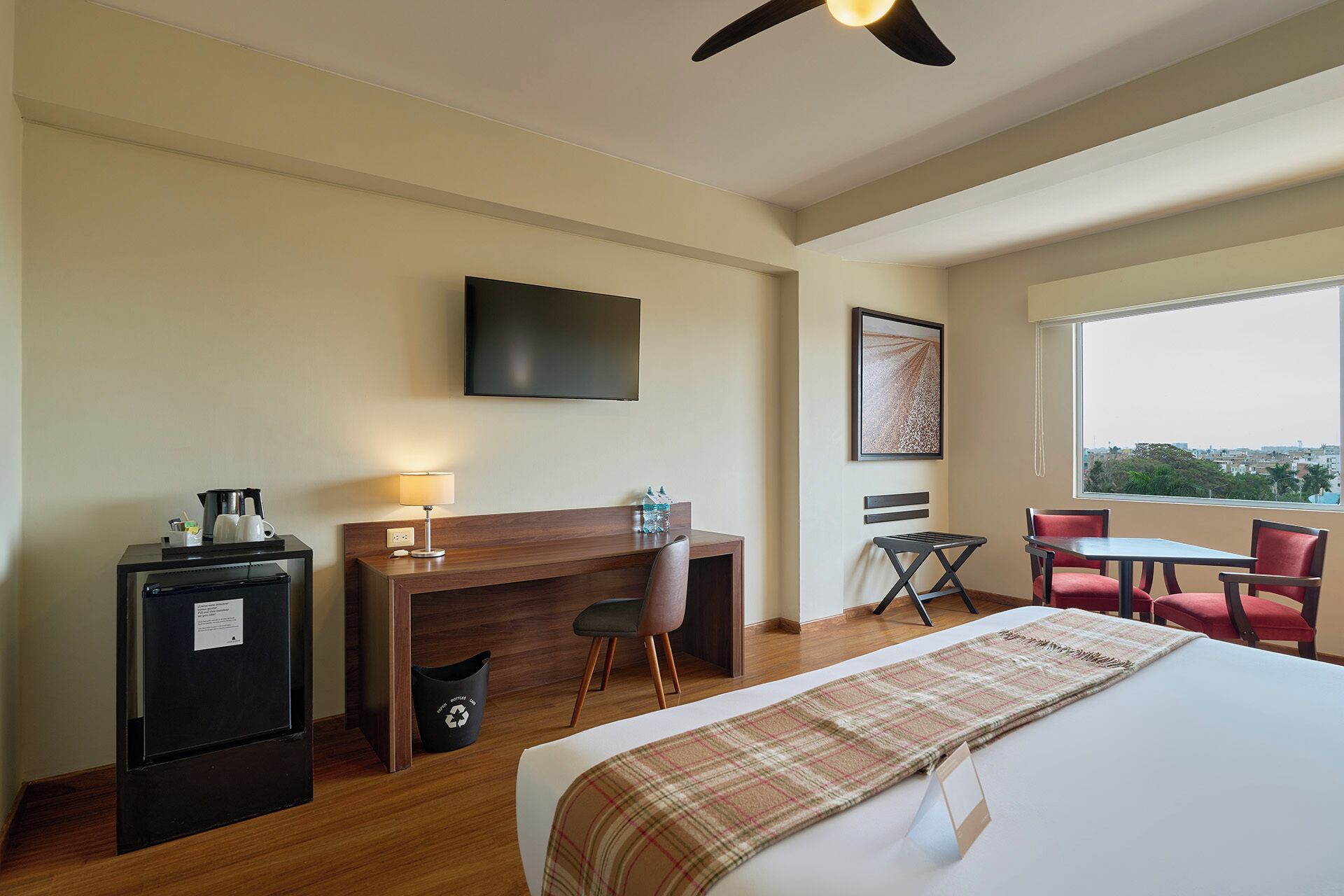 A hotel room with a bed, a desk, a chair, a TV, and a window with a view.