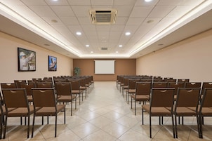 A conference room with rows of chairs, a projector screen, and two framed pictures on the wall.