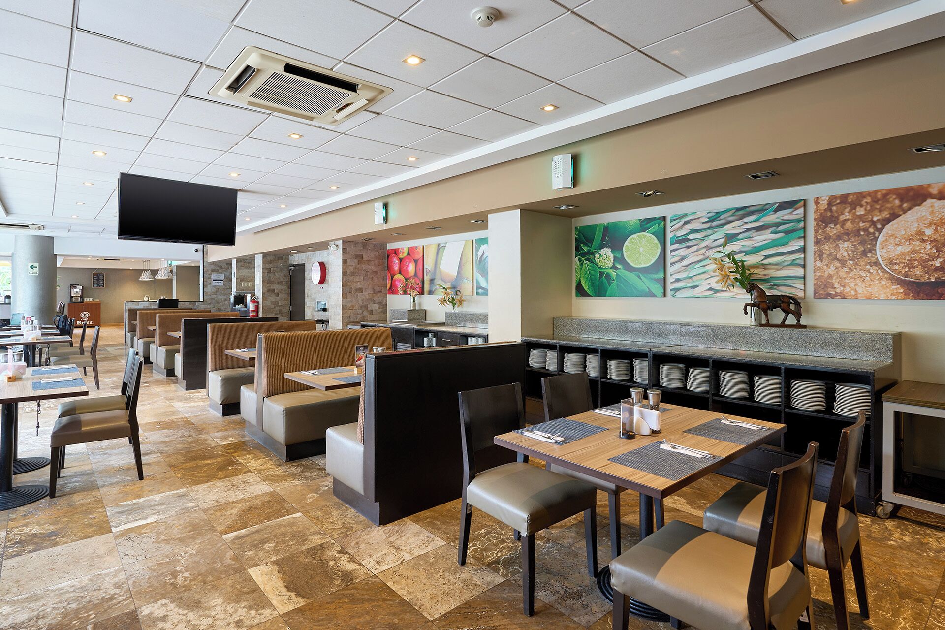 A restaurant with booth seating, tables with place settings, and a flat-screen TV mounted on the ceiling.