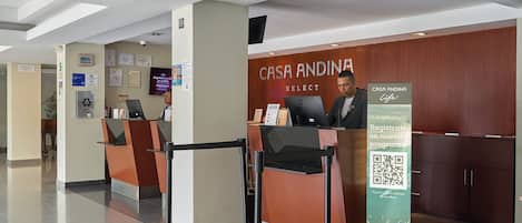 A reception area with a counter, a sign for 'CASA ANDINA SELECT', and a QR code for program registration.
