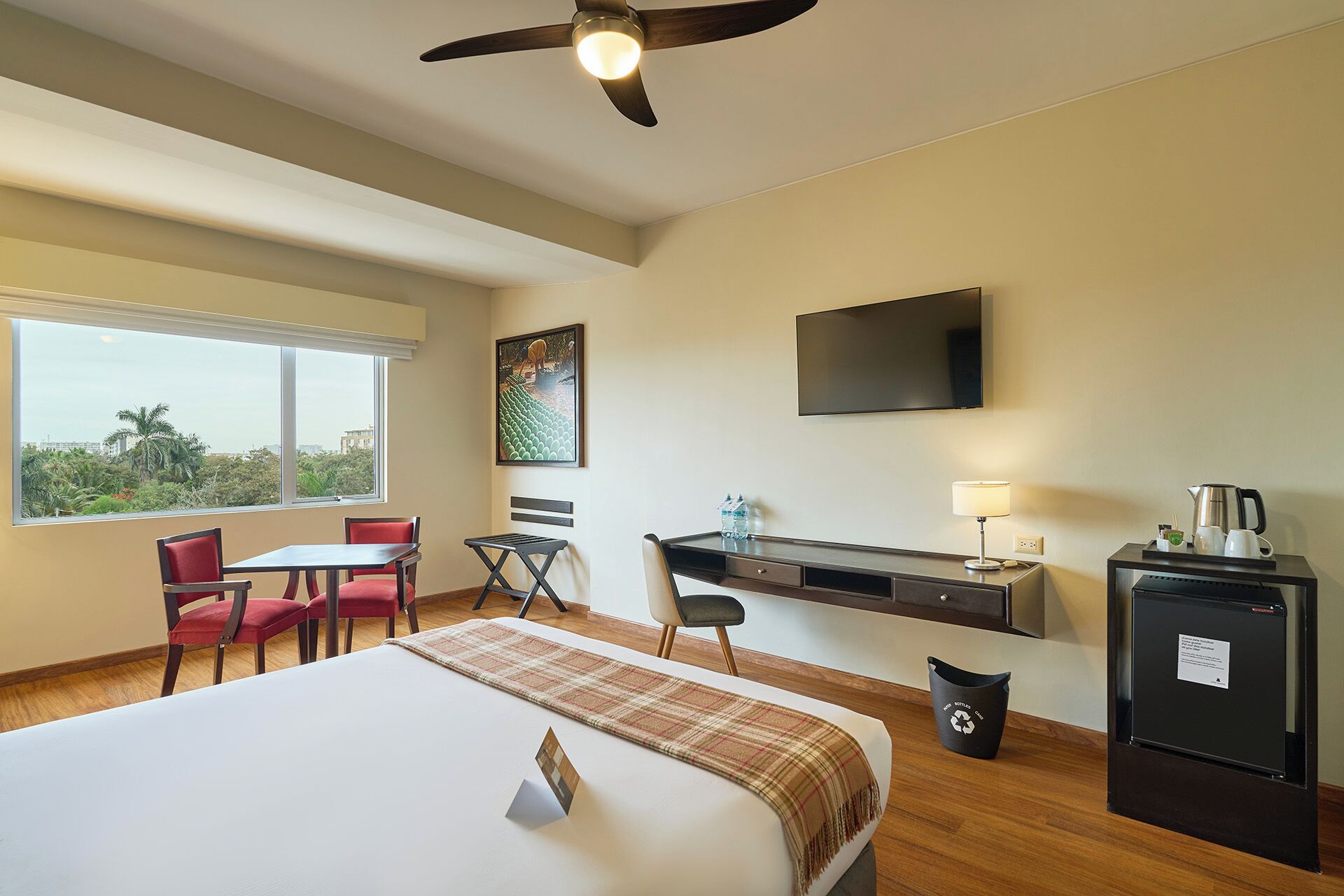 A hotel room with a bed, desk, chairs, a television, and a view of the outdoors.