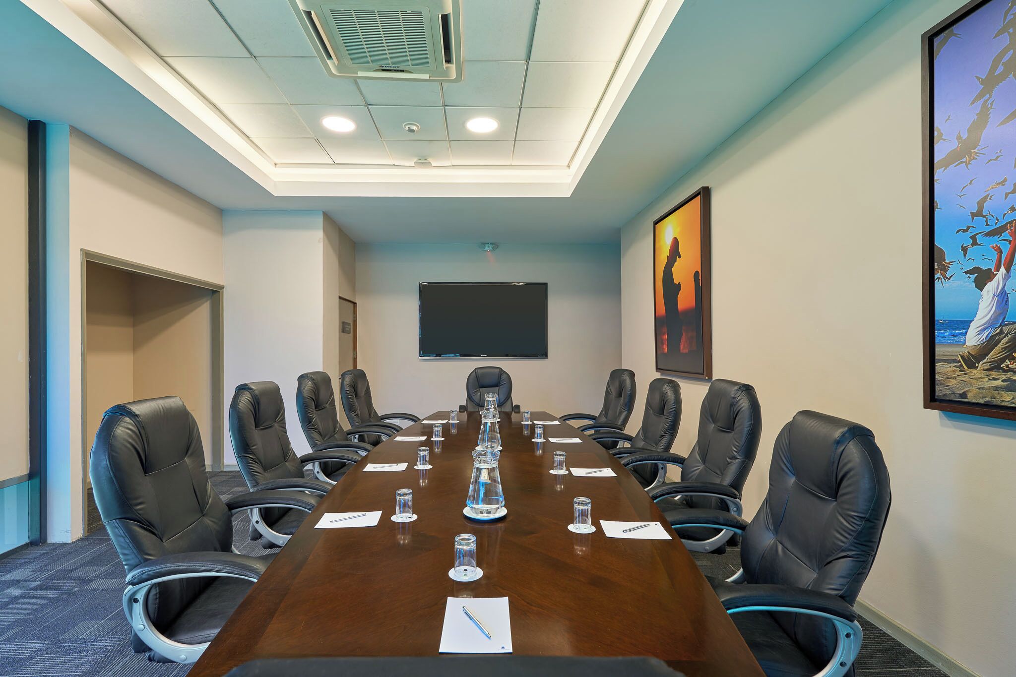 A conference room with a long table, chairs, a projector screen, and artwork on the walls.