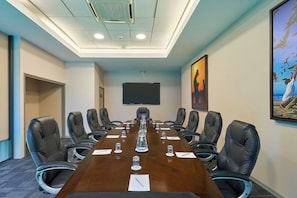 Una sala de conferencias con una mesa larga, sillas, una pantalla de proyector y obras de arte en las paredes.